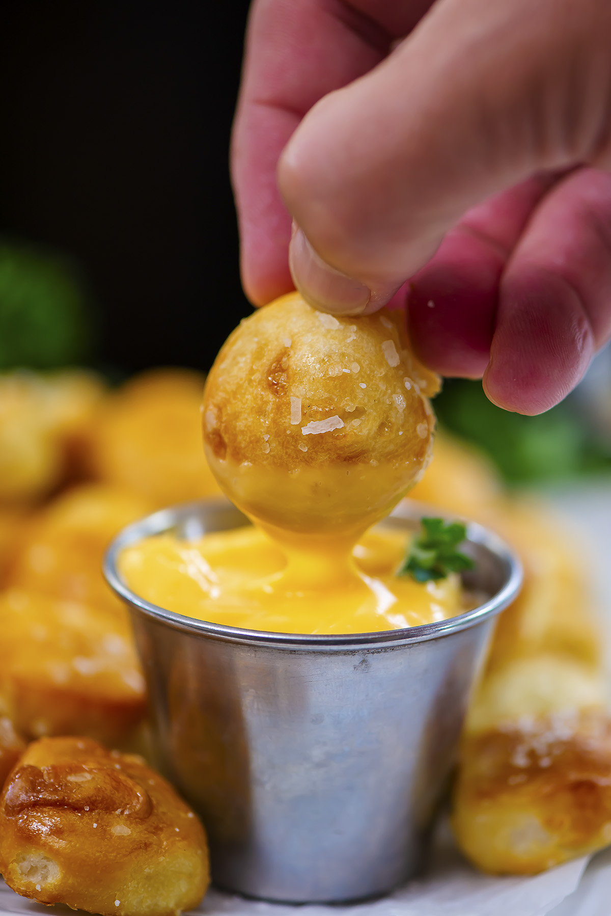 Close up of a salted pretzel bite being dipped into cheese.