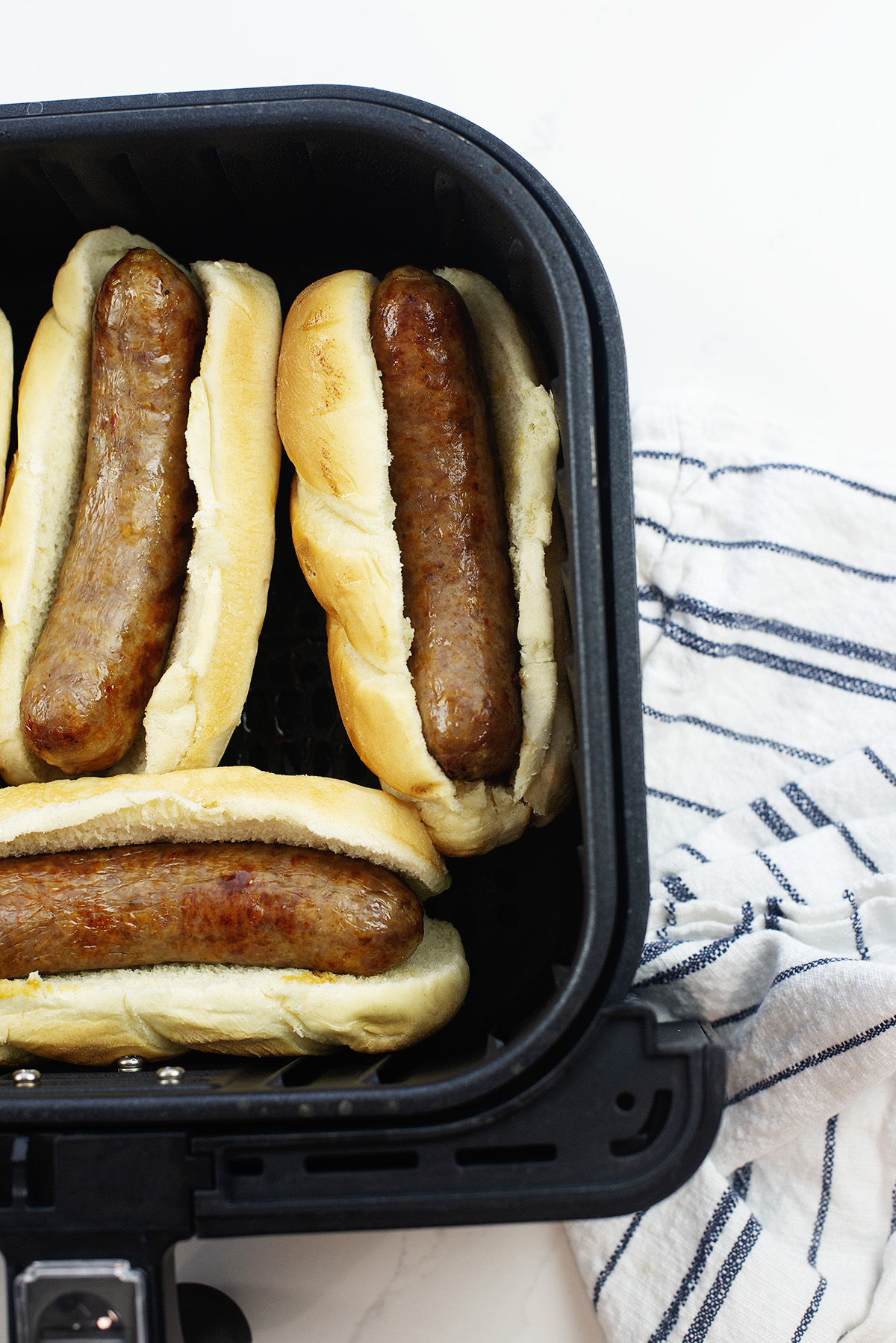 A few Italian sausages on buns in an air fryer basket.
