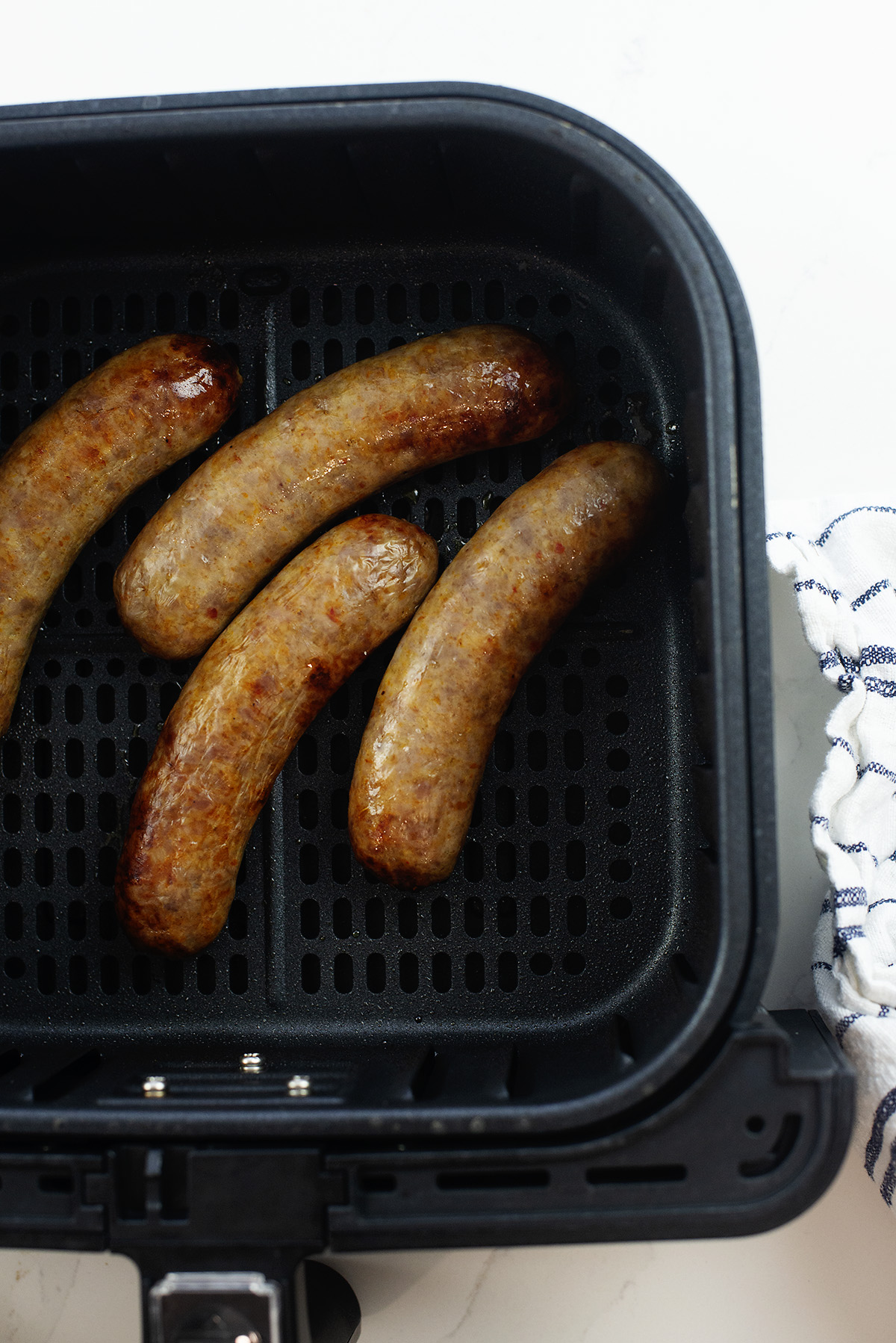 Four Italian sausages in an air fryer basket.