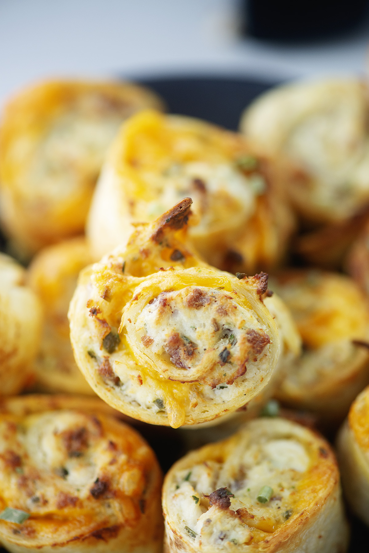 Close up of a cheesy chicken pinwheel on top of more chicken pinwheels.