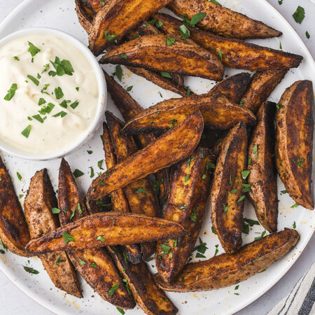 Sweet potato wedges on white plate with bowl of dip.