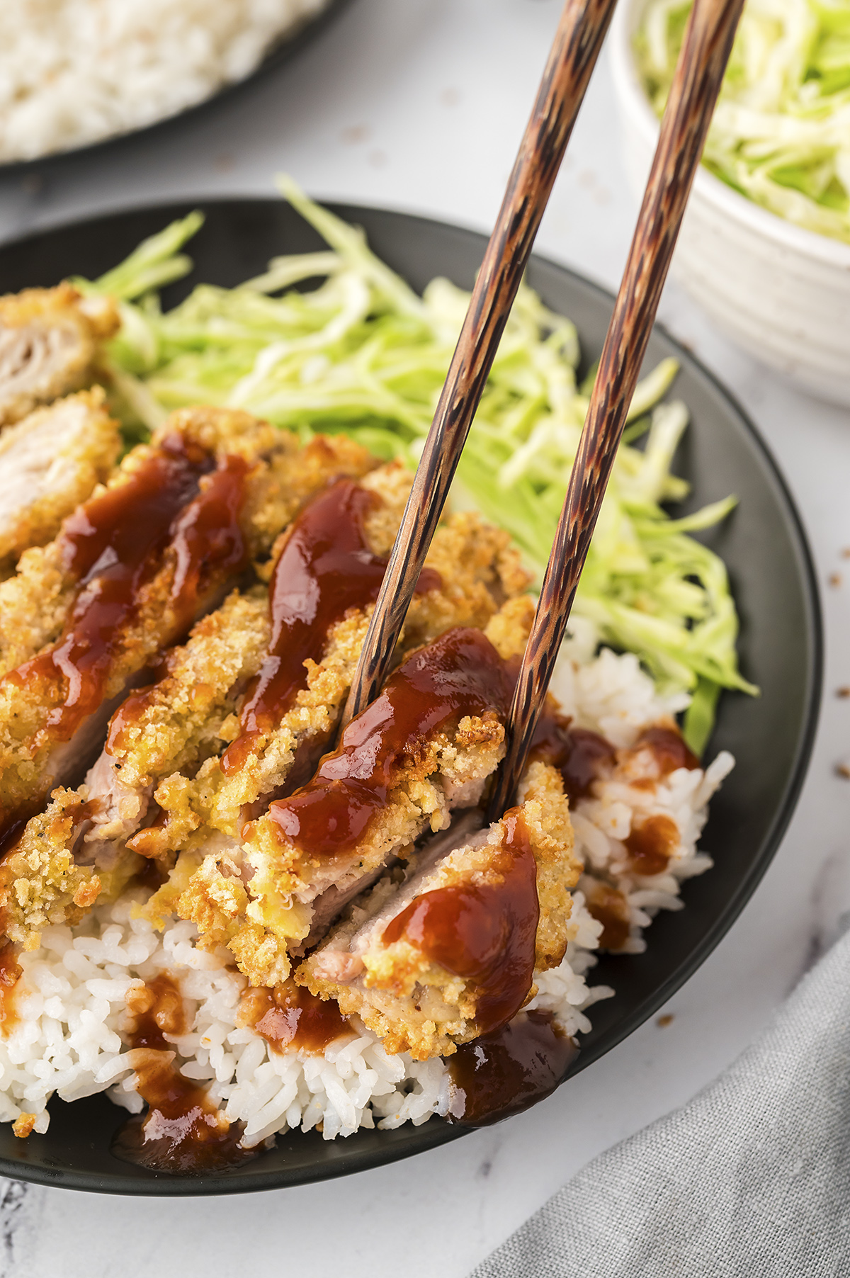 Chicken katsu served in a black bowl with rice and noodles.