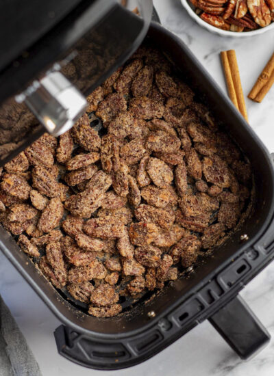 A partially open air fryer with cooked candied pecans.