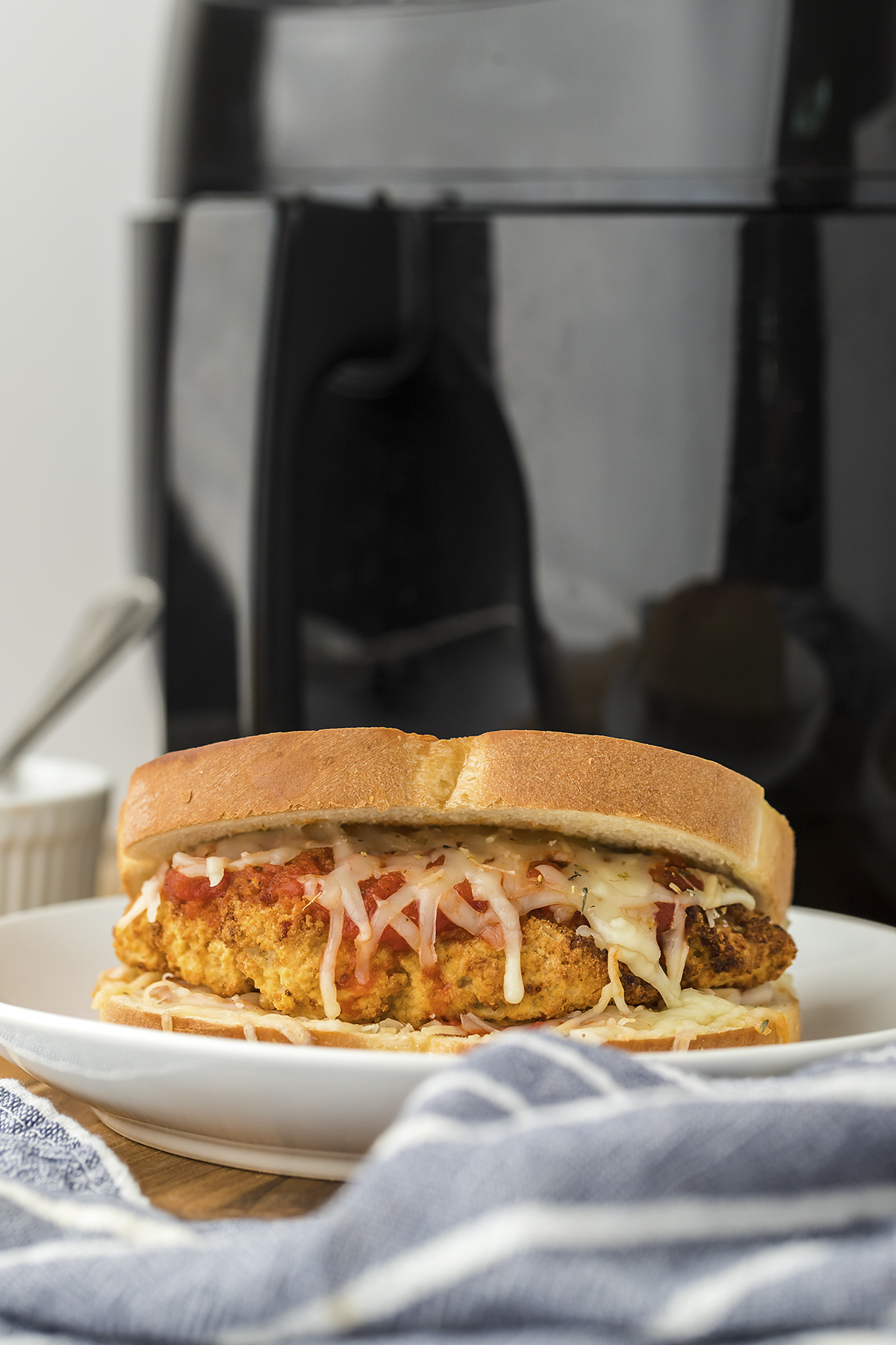 Chicken parmesan sandwich on white plate in front of air fryer.