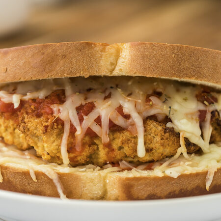 Close up of chicken parmesan sandwich on white plate.