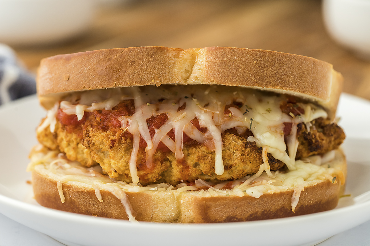 Close up of chicken parmesan sandwich on white plate.