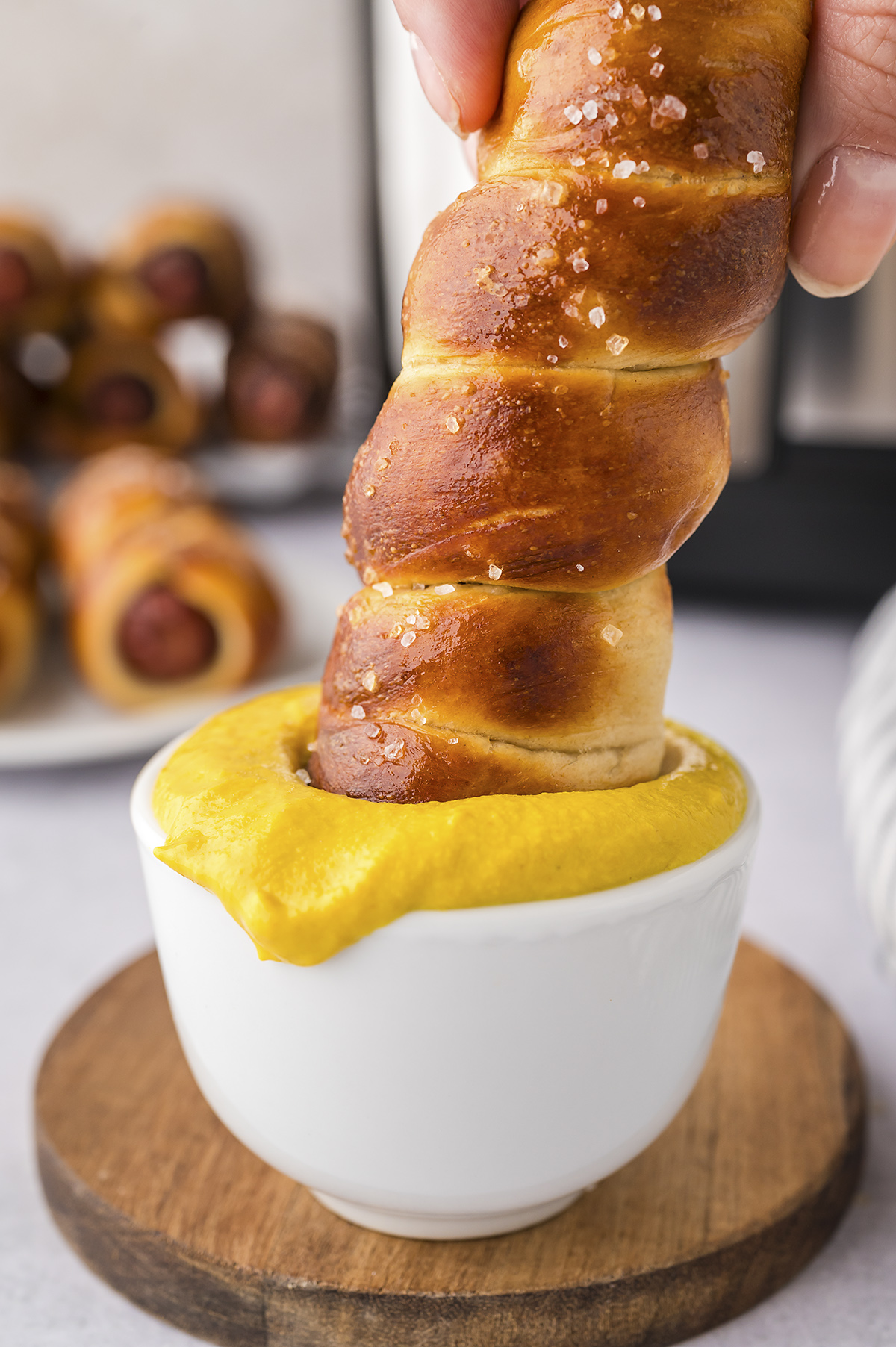 A pretzel dog being dipped into mustard.