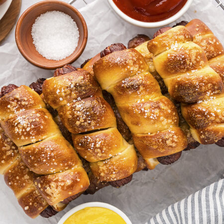 Many pretzel dogs stacked up in a row.