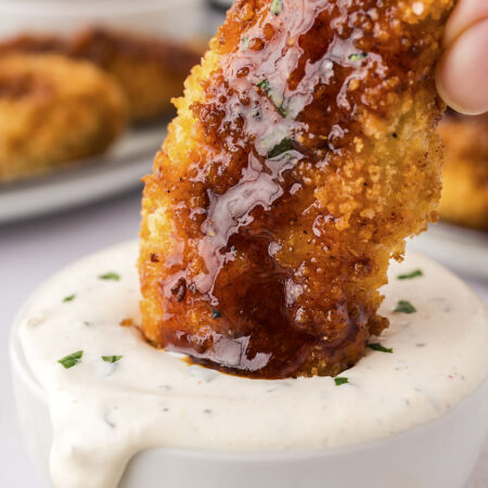 Up close picture of a person dipping a hot honey chicken strip into ranch dip.