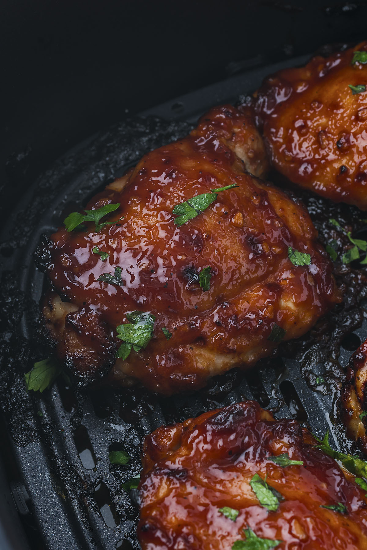 A close up of BBQ chicken thighs, garnished, in an air fryer basket.
