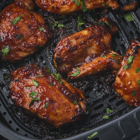 Close up of several chicken thighs in an air fryer basket.