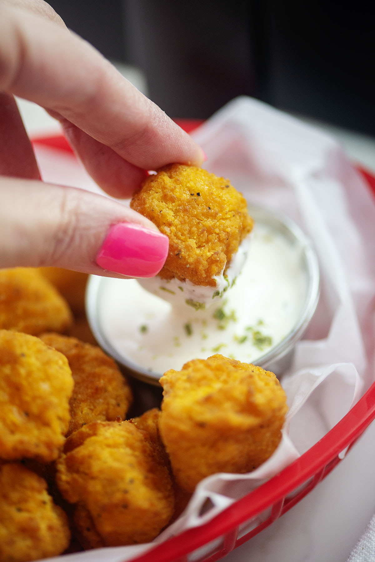 Woman's hand dipping a piece of popcorn chicken into ranch dressing.