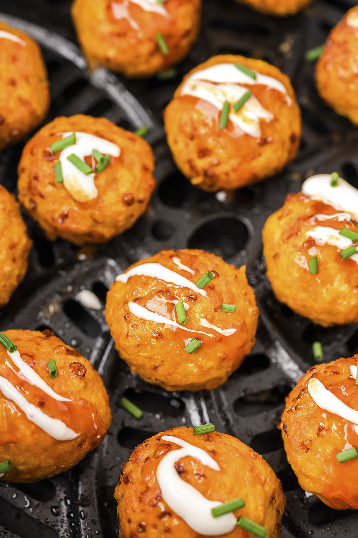 Close up of cooked Buffalo chicken meatballs in an air fryer basket.