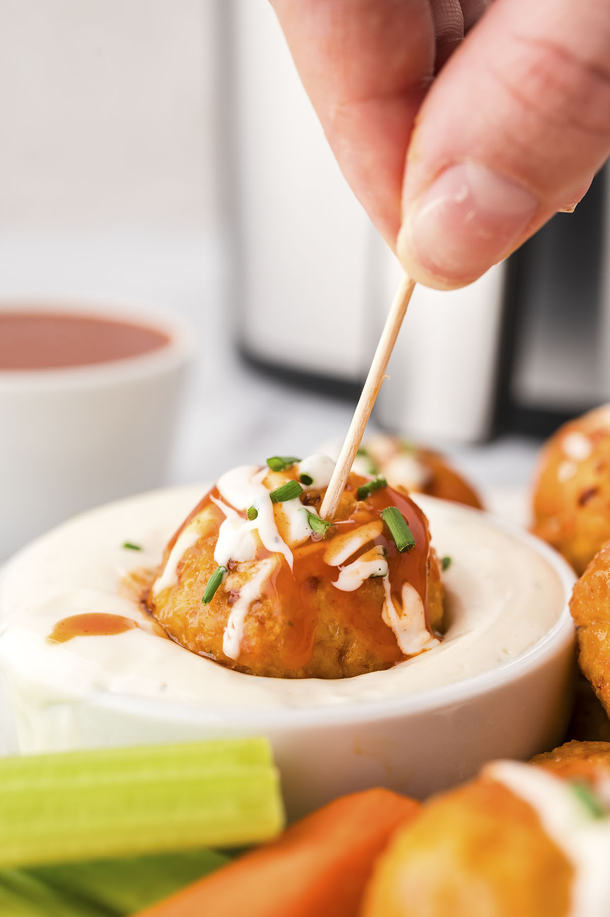 A close up of a Buffalo chicken meatball being dipped in ranch dressing.