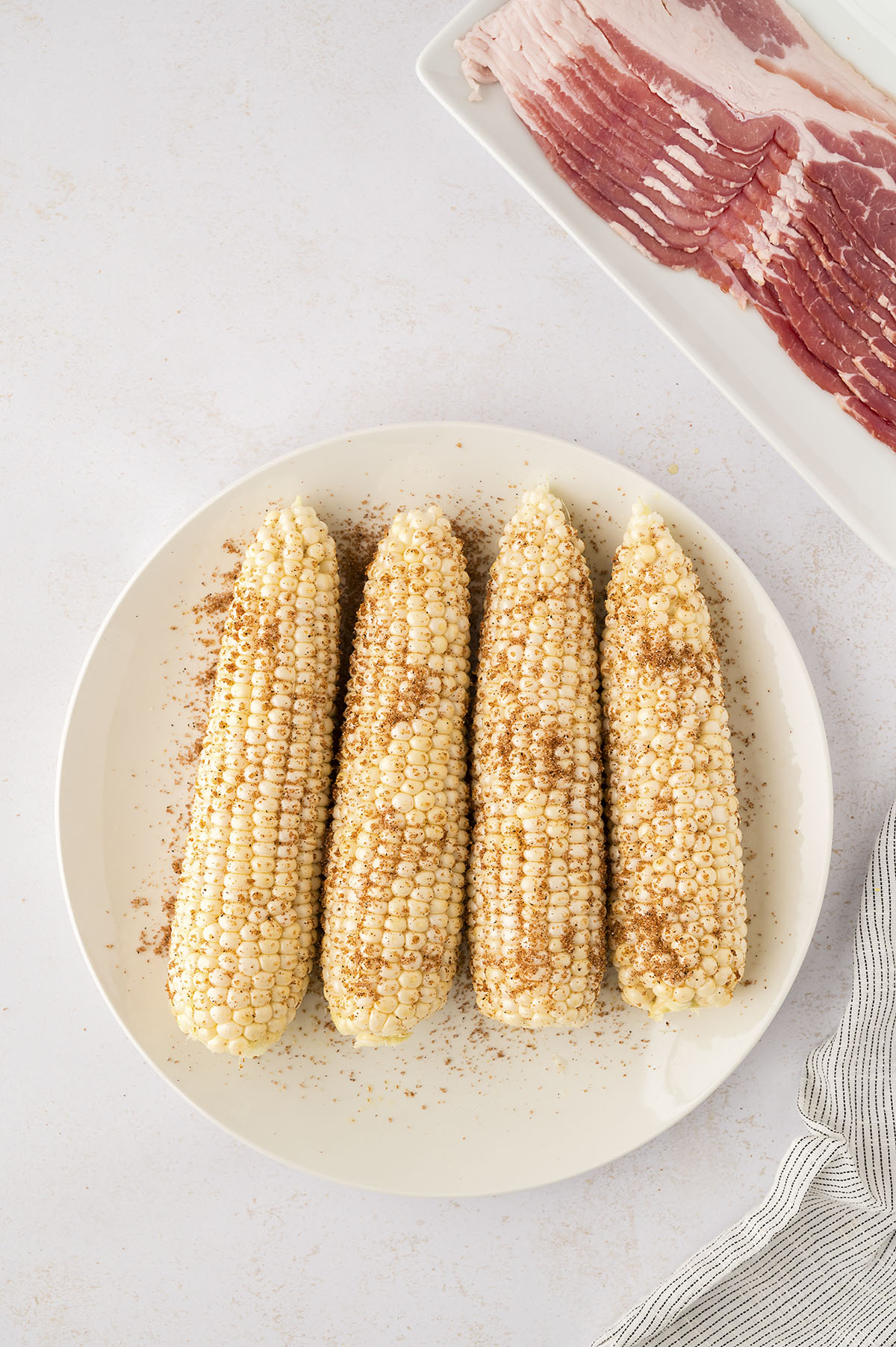 Four seasoned corn cobs on a white plate.