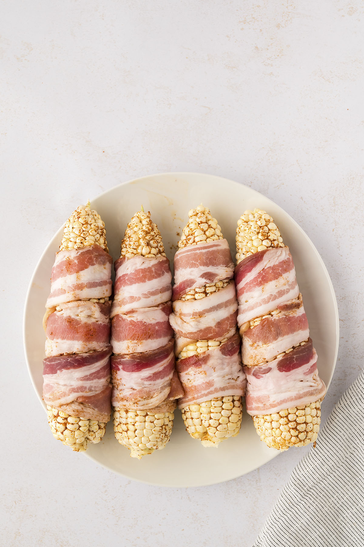Four corn cobs wrapped in raw bacon.