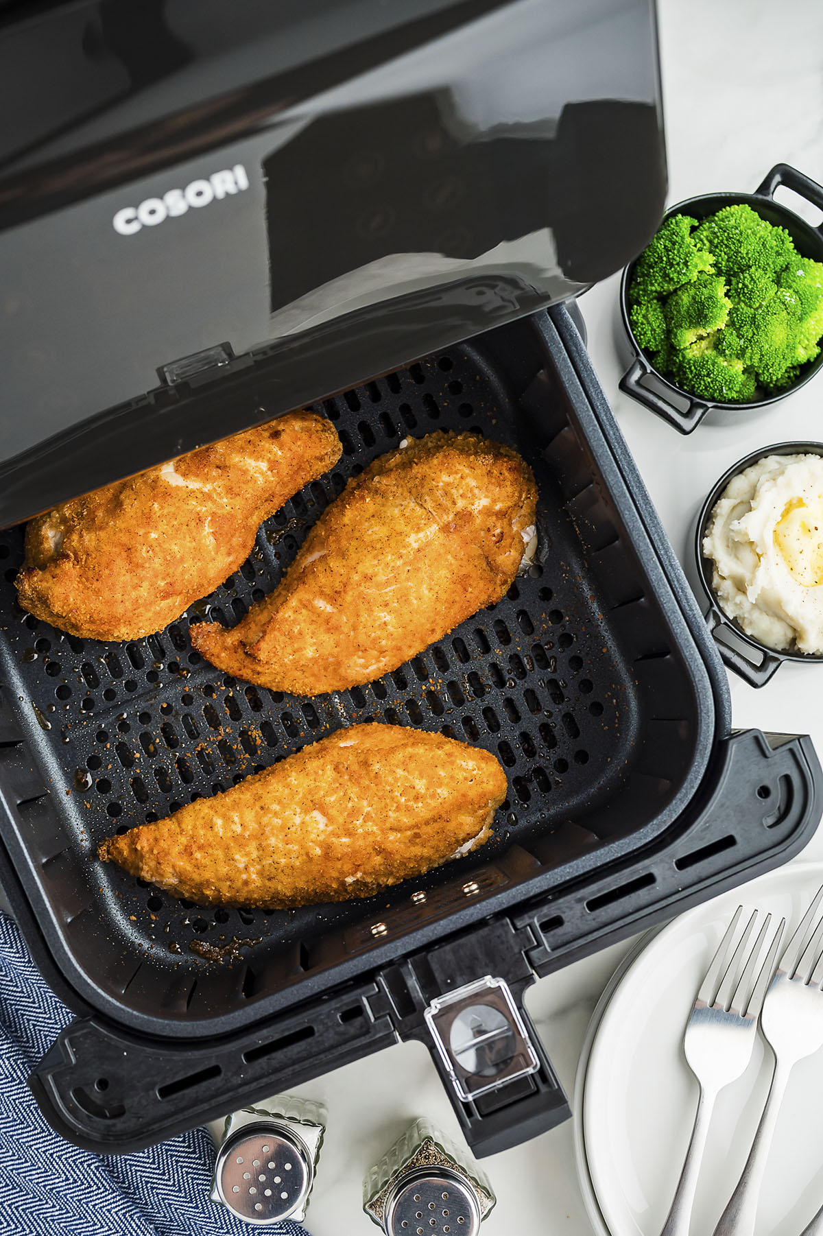 An air fryer basket with chicken in it partially open.