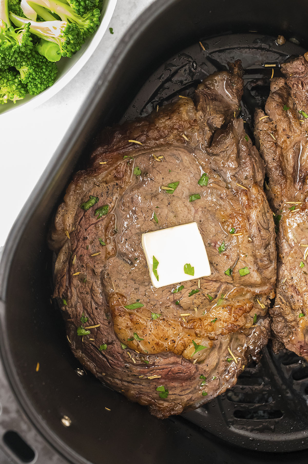 Close up of an air fryer basket full of ribeye steaks.