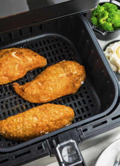 Three pieces of cooked shake and bake chicken in an air fryer basket.
