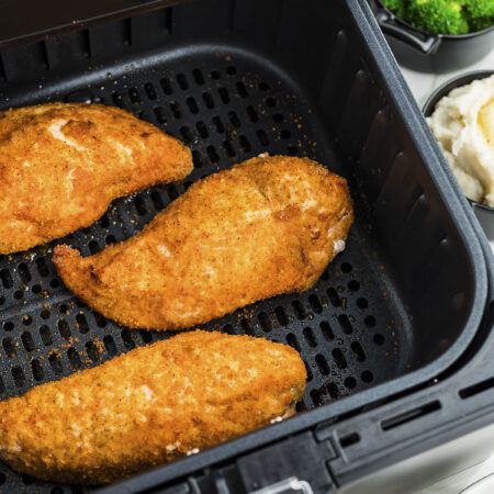 Three pieces of cooked shake and bake chicken in an air fryer basket.