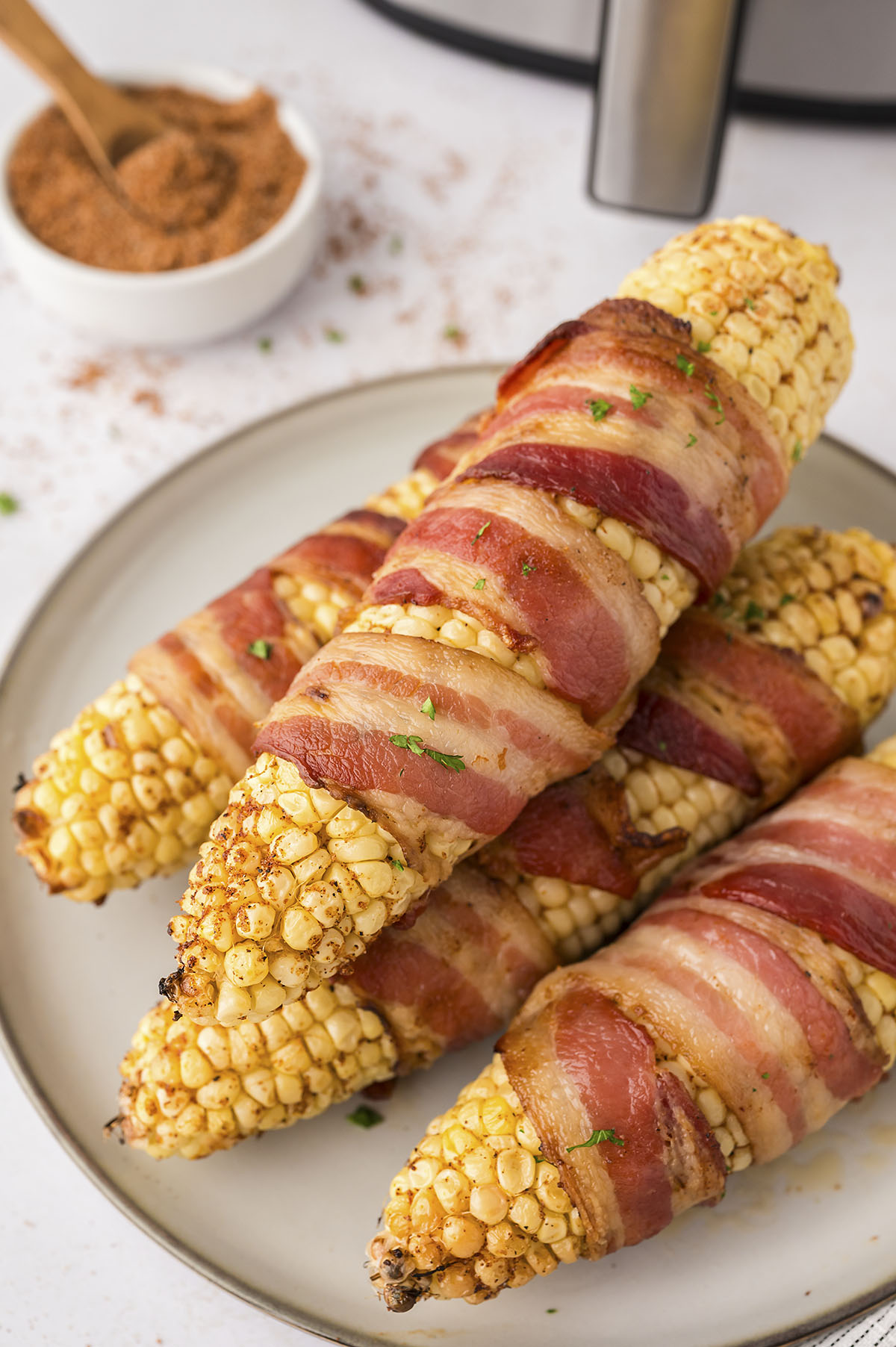 A plate with four bacon wrapped corn on the cobs on it.