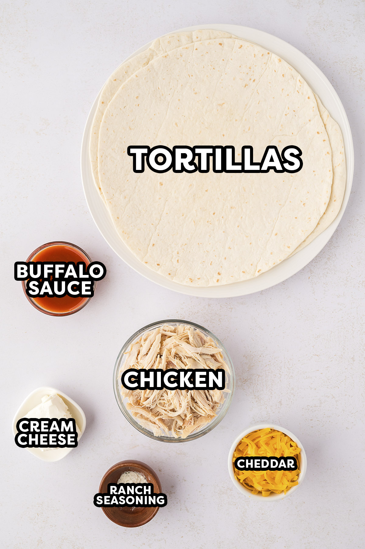 Ingredients needed to make buffalo chicken pinwheels on a white countertop.