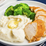 A white dish with mashed potatoes and chicken.