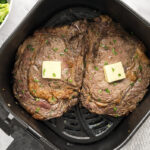 Two ribeyes in an air fryer basket.