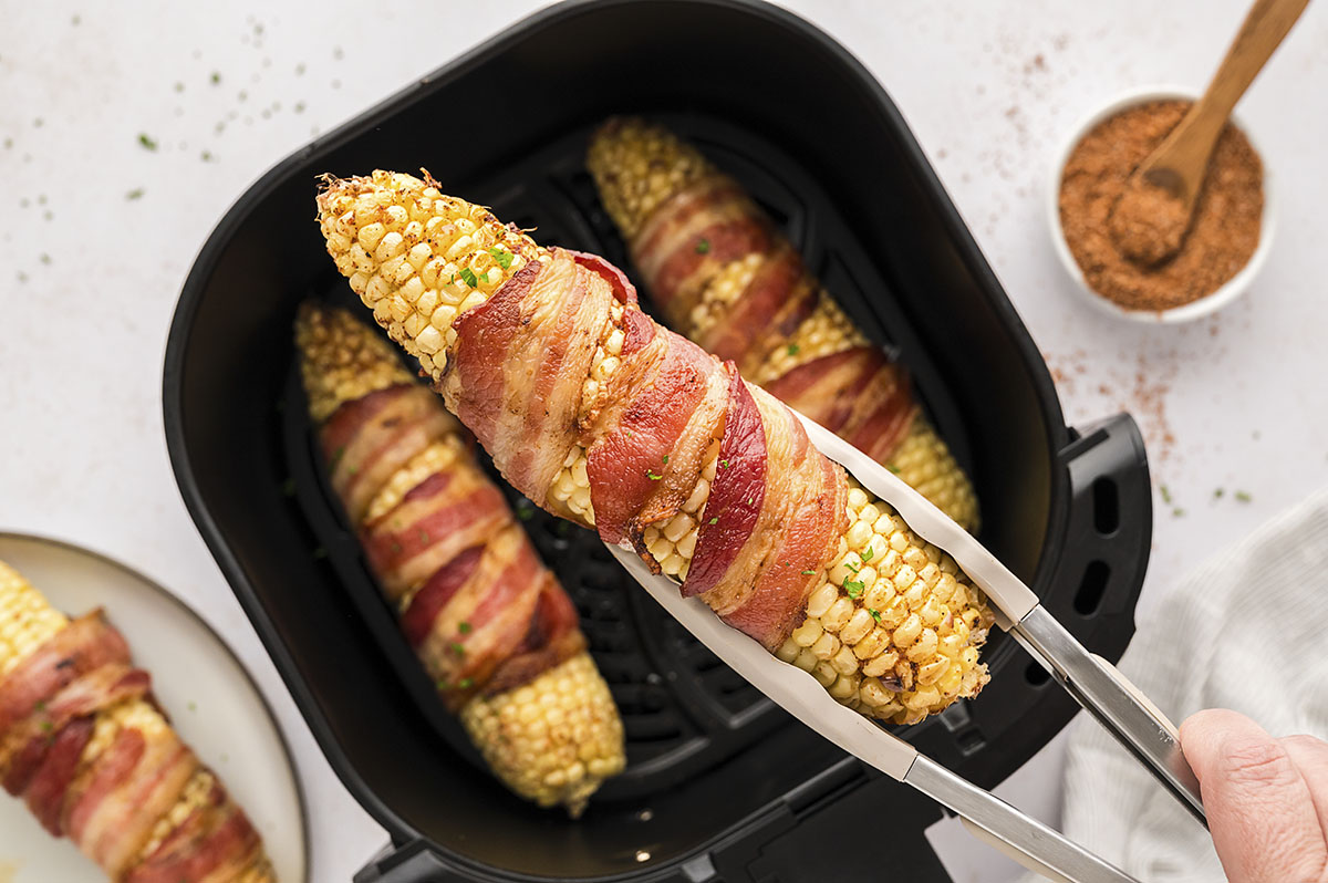 Bacon wrapped corn being held by tongs.