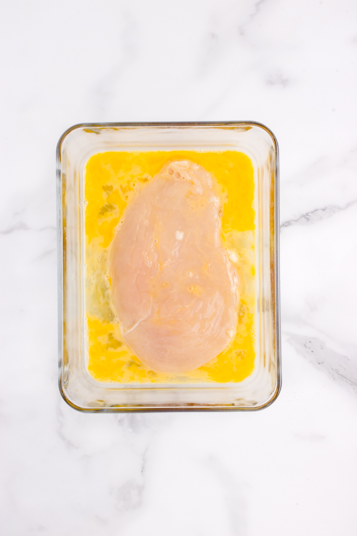 Chicken breast being dipped in egg.