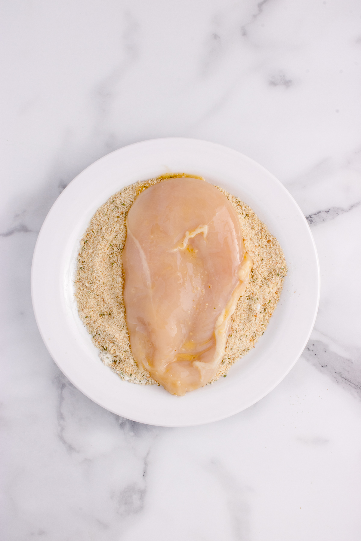 Chicken breast on plate of breadcrumbs.