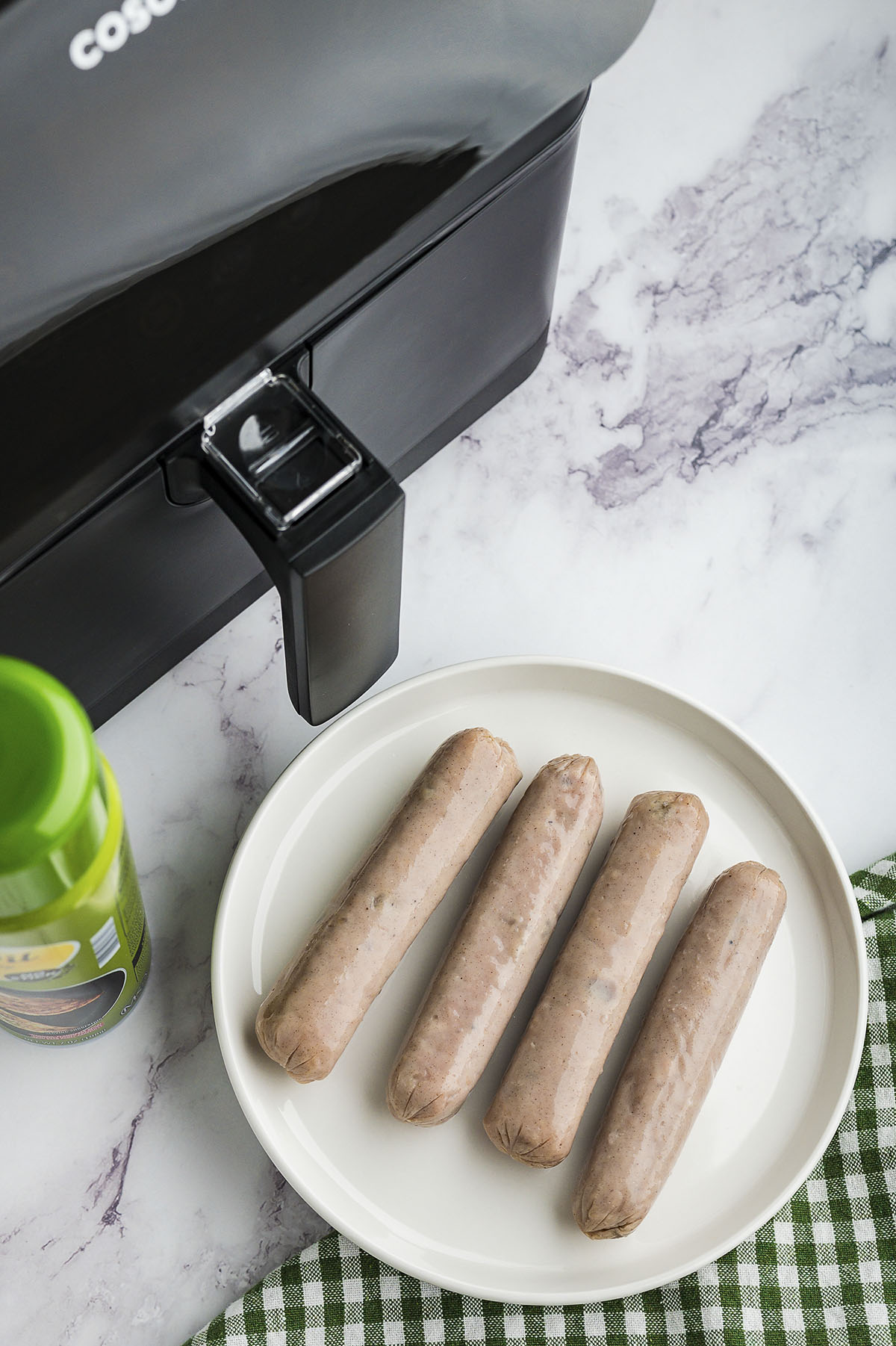 Uncooked chicken sausages on plate next to air fryer.