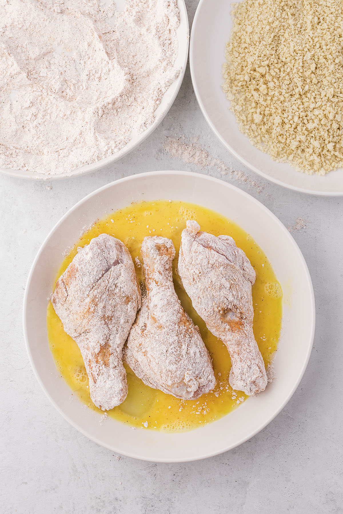 Floured chicken legs being dipped in egg.