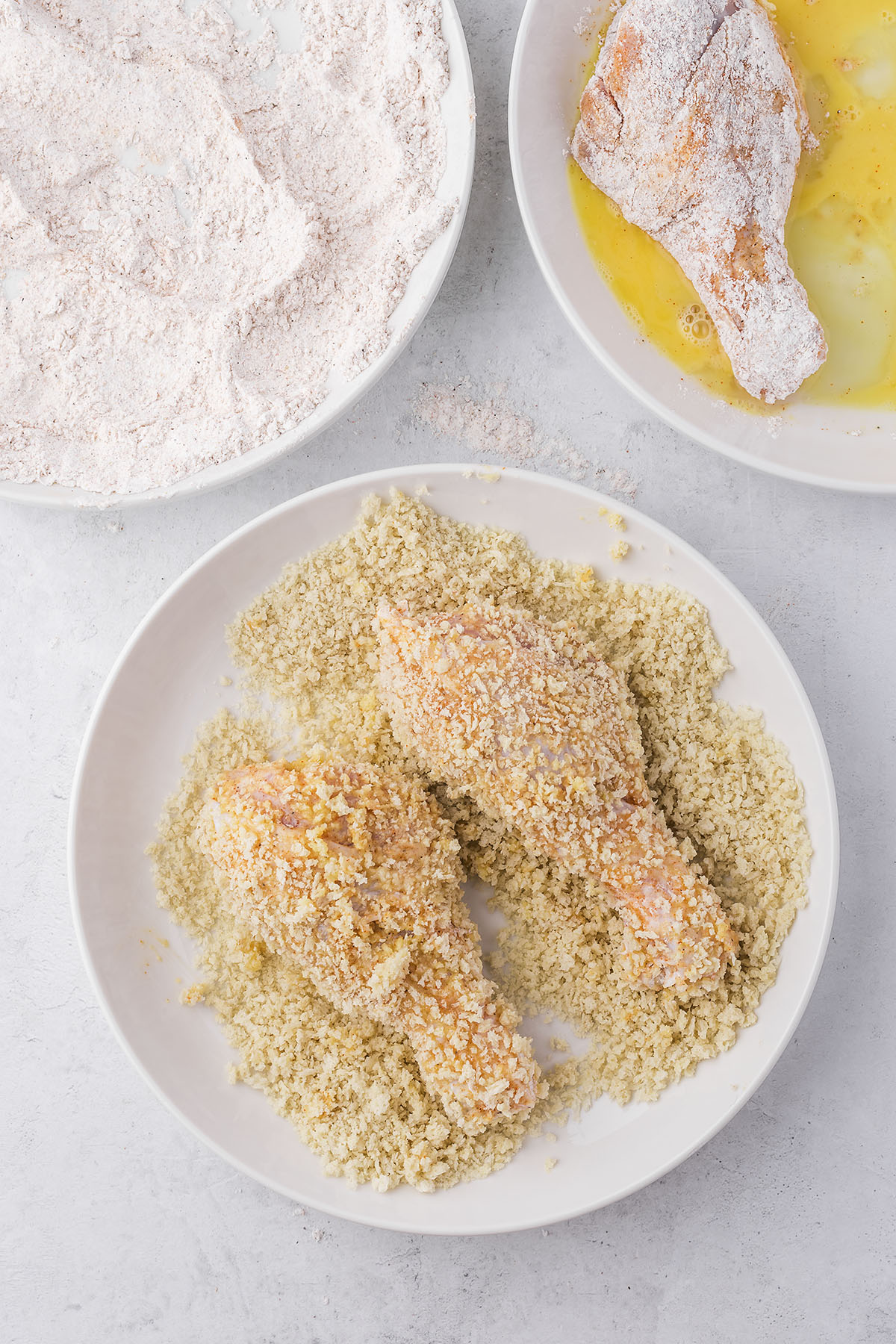 Chicken legs being coated in bread crumbs.