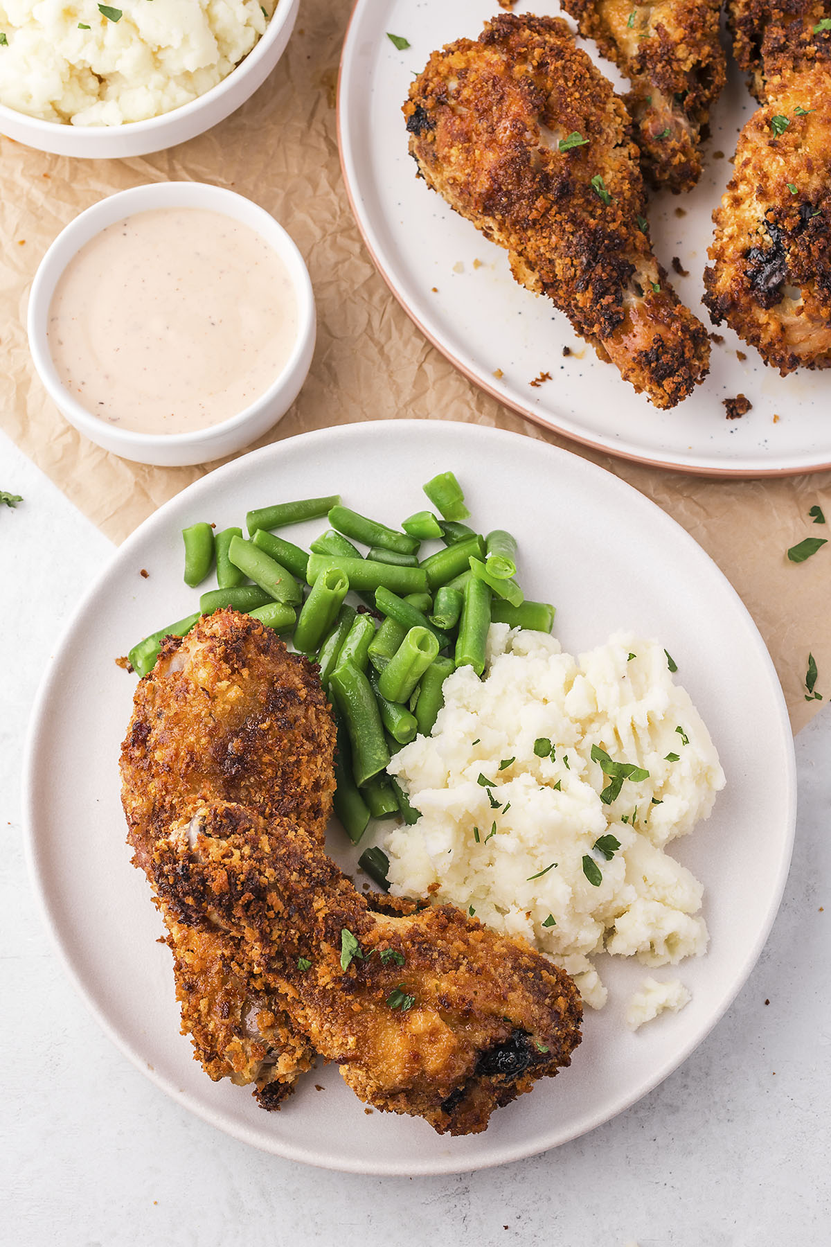 Breaded chicken legs on plate with mashed potatoes and green beans.