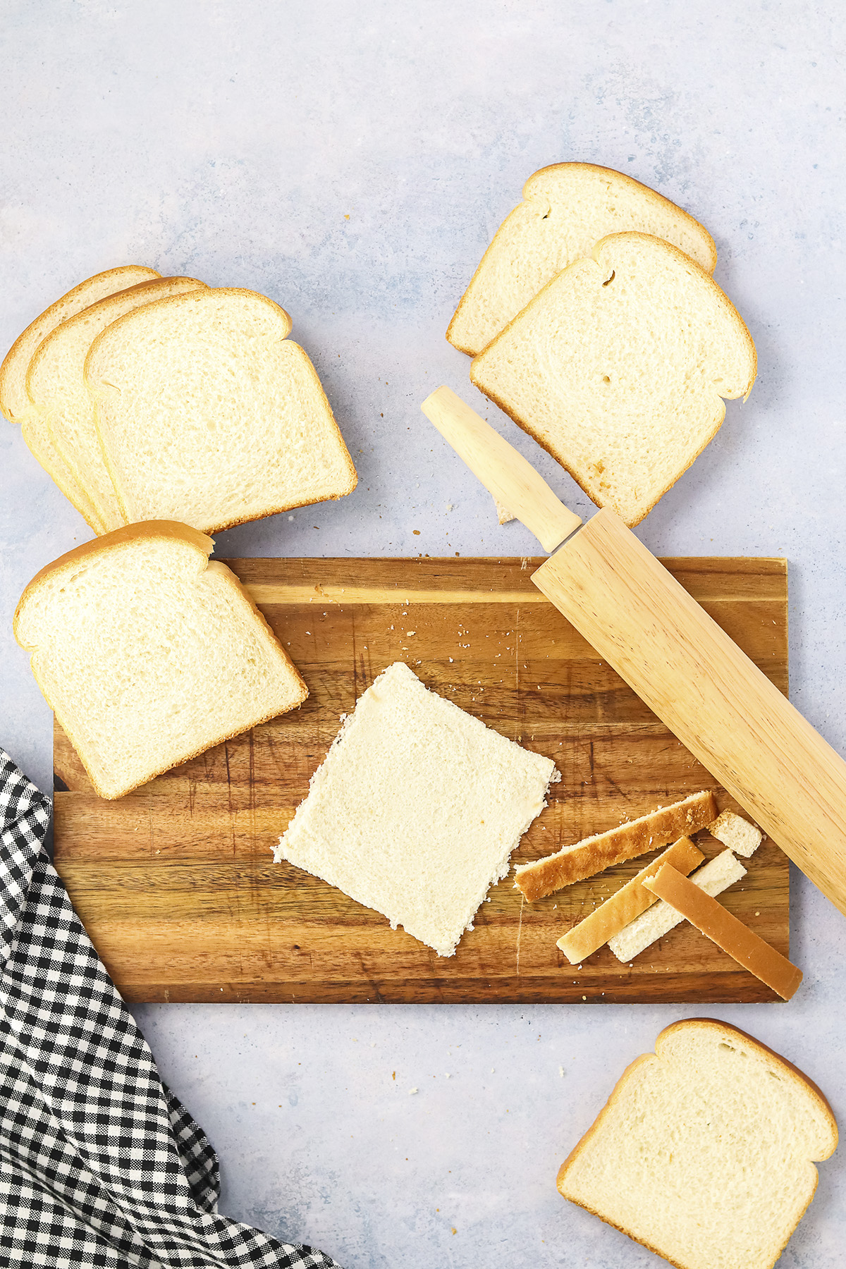 Crust cut off bread and bread flattened on wooden cutting board.