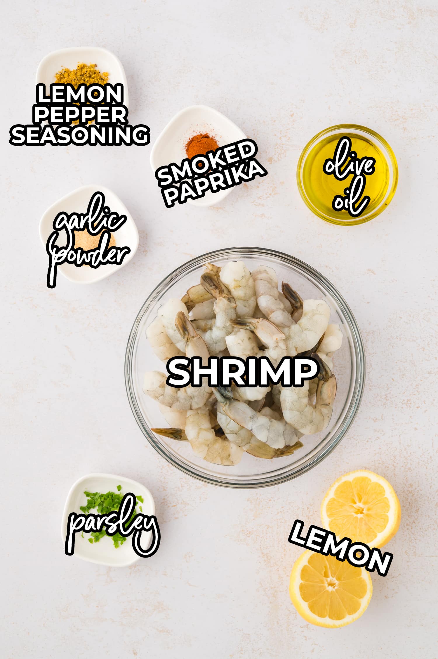Ingredients for lemon pepper shrimp spread out on a white countertop and labeled.