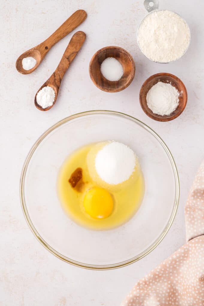 The ingredients for two snickerdoodle cookies are being mixed together in a clear glass bowl.