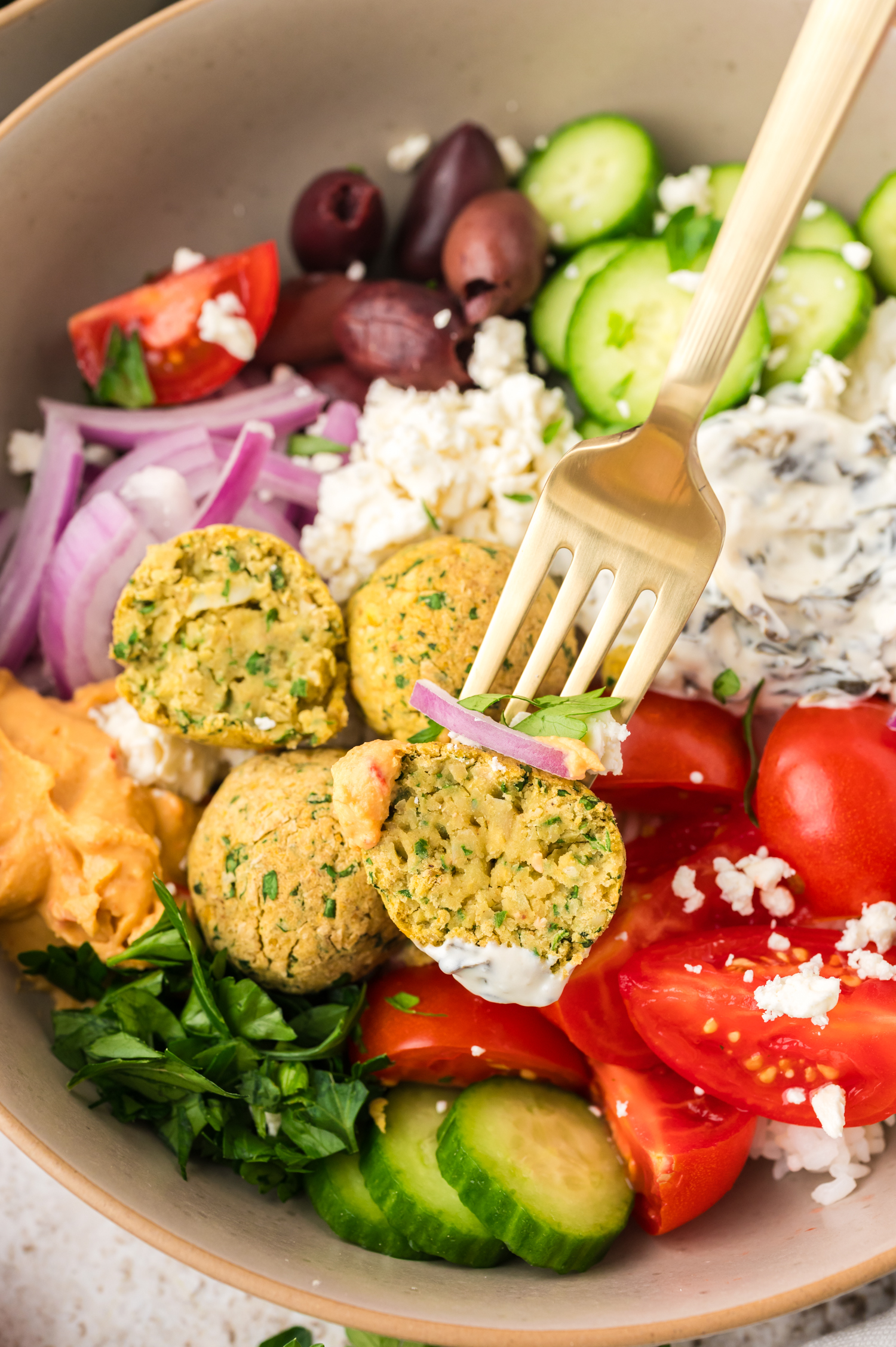 Half a falafel on a fork in a falafel bowl.