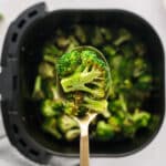 A spoonful of cooked broccoli over an air fryer basket.