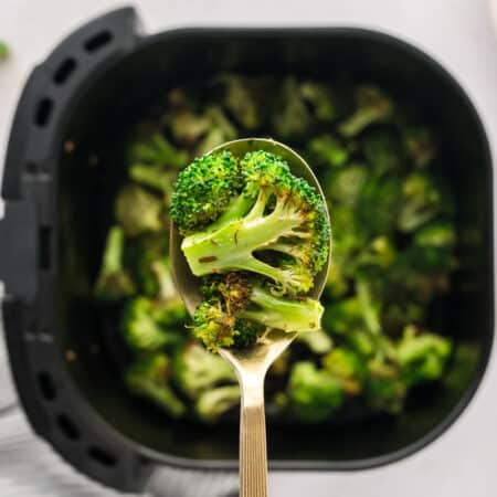 A spoonful of cooked broccoli over an air fryer basket.