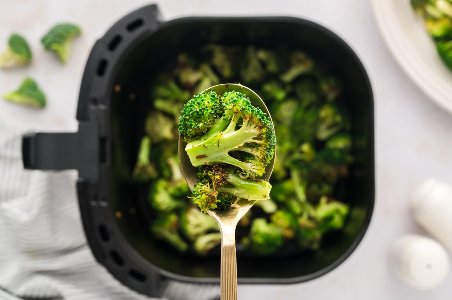 A spoonful of cooked broccoli over an air fryer basket.