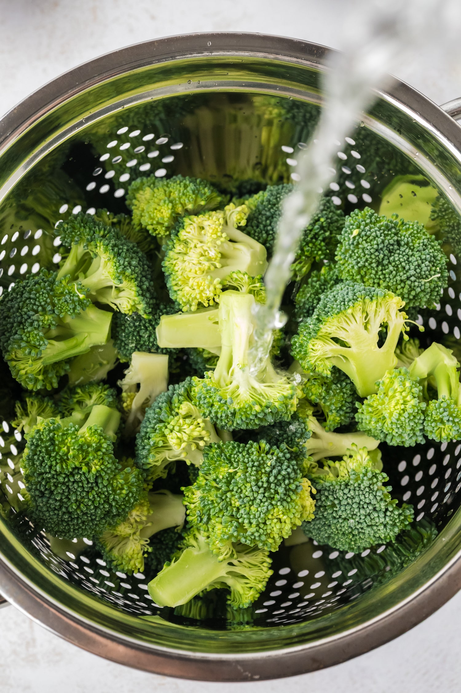 Raw broccoli being rinsed in a strainer.