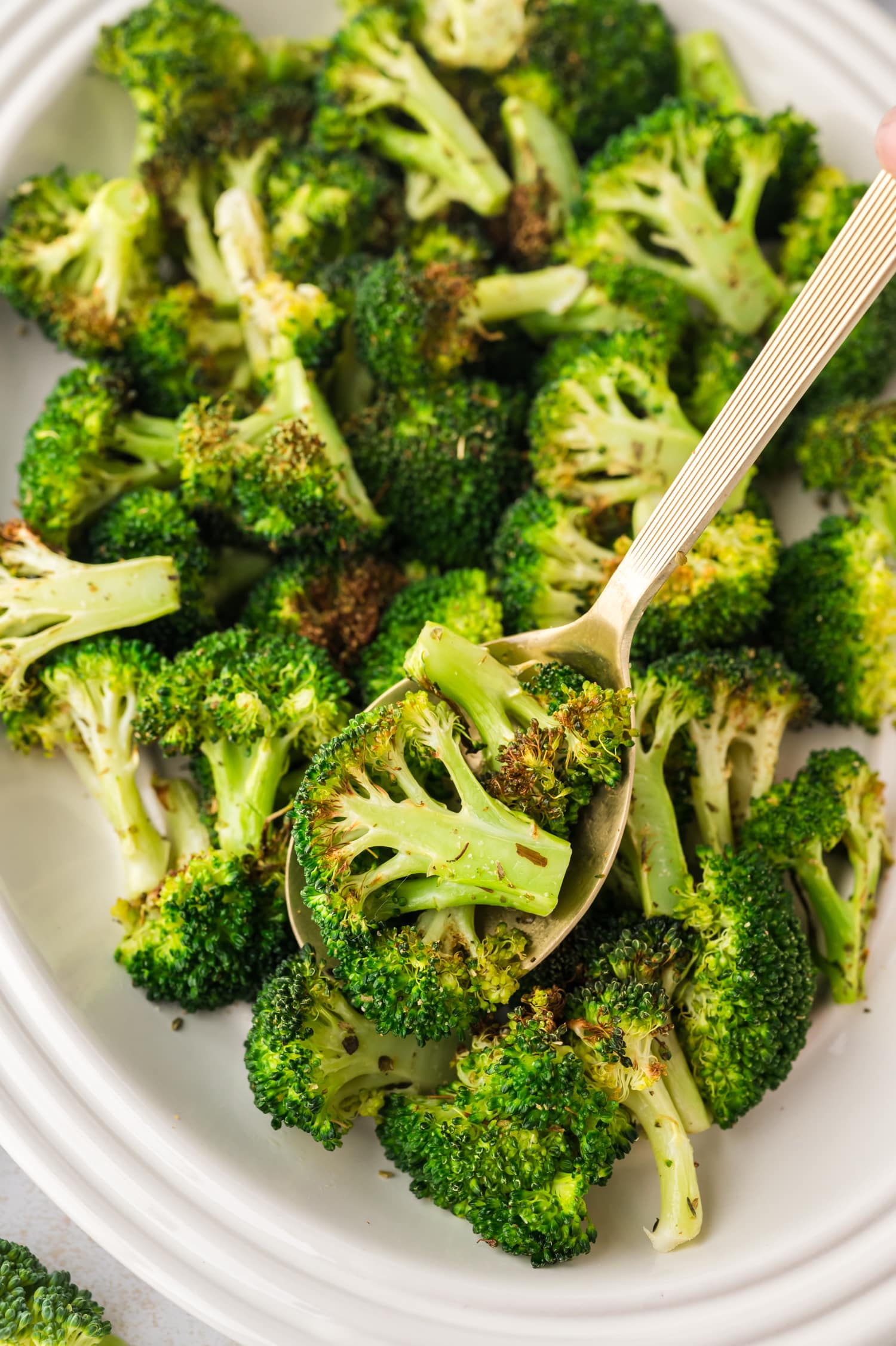 A spoon scooping a piece of broccoli off of a plate.