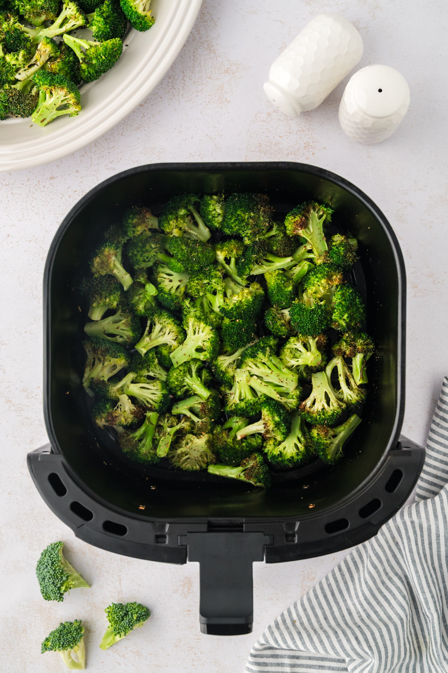 Overhead view of an air fryer basket full of cooked broccoli.