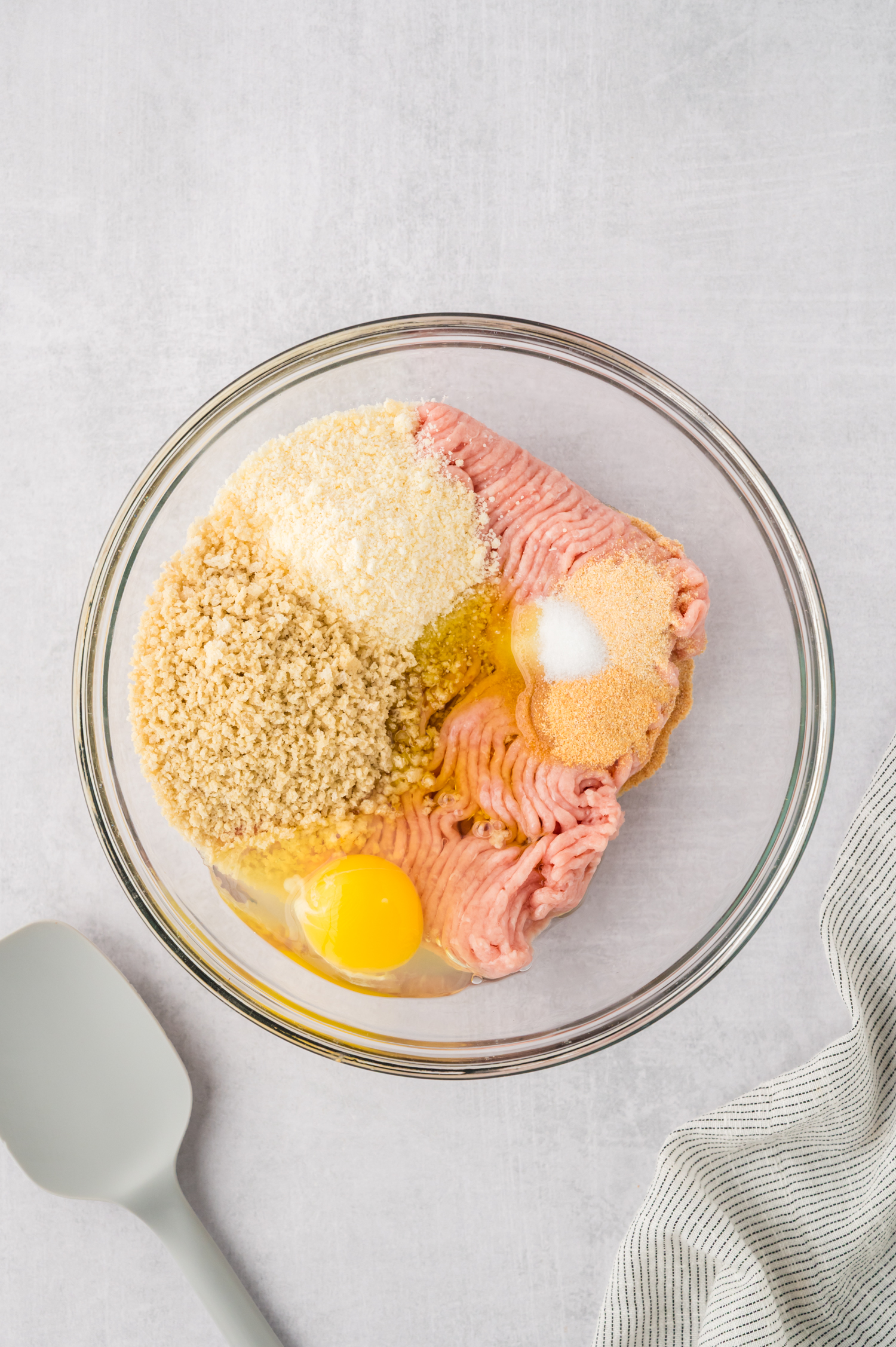 A clear glass bowl with unmixed chicken meatball ingredients in it.