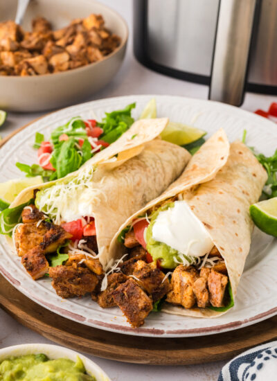 A plate With two Chipotle chicken burritos on it sitting in front of an air fryer basket.