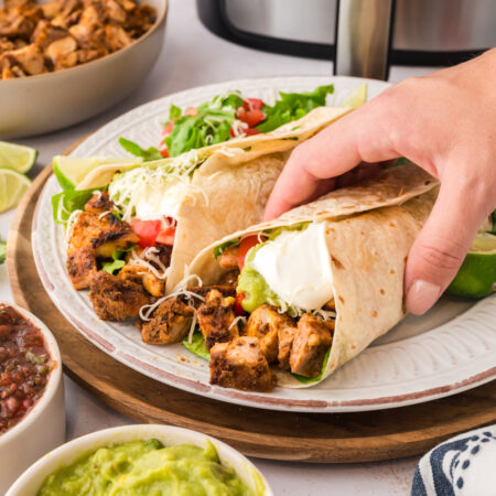 A person grabbing a Chipotle chicken burrito off of a plate.