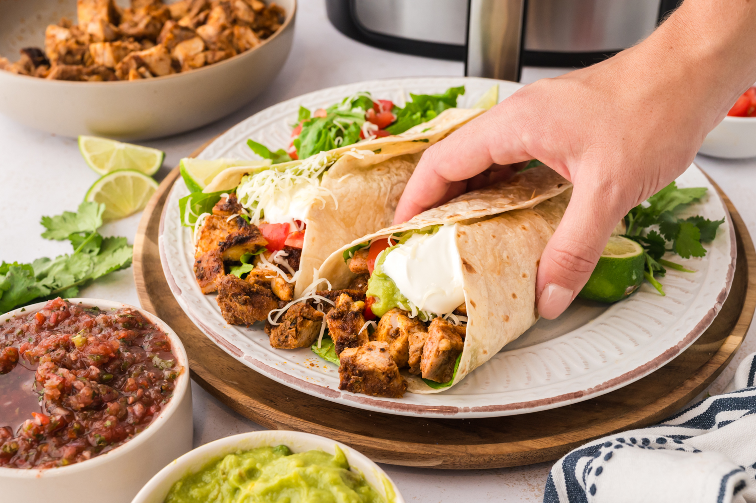 A person grabbing a Chipotle chicken burrito off of a plate.