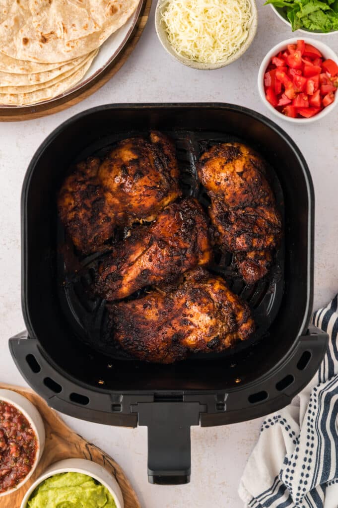 Four cooked Chipotle chicken thighs and an air fryer basket.